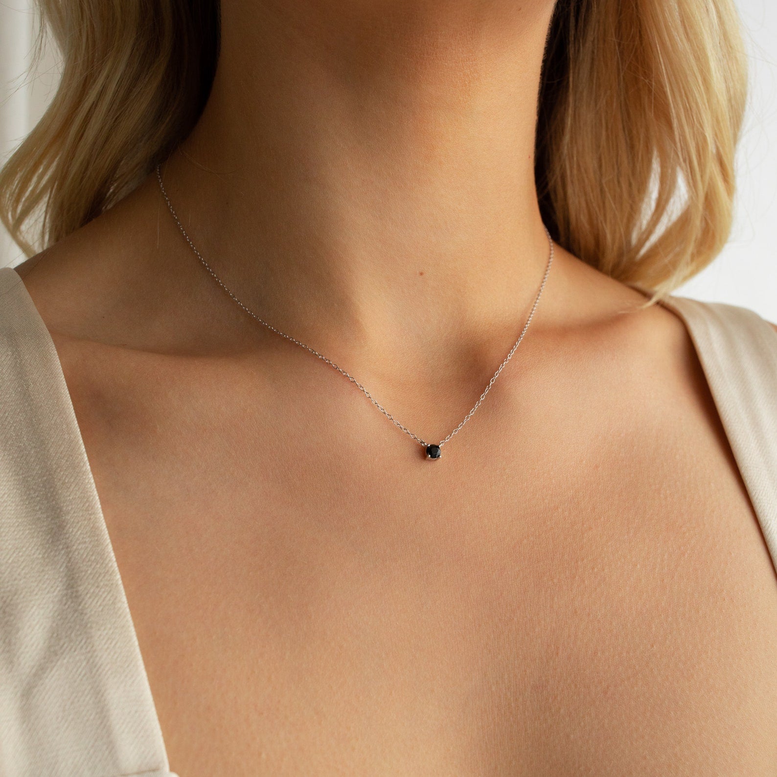 A woman wearing the Onyx Dainty Diamond Necklace—a delicate silver chain with a small black stone pendant—adds timeless elegance to her look.