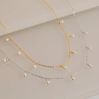 Gold and silver chain necklaces, each adorned with evenly spaced small white pearl drops, displayed on a light surface.