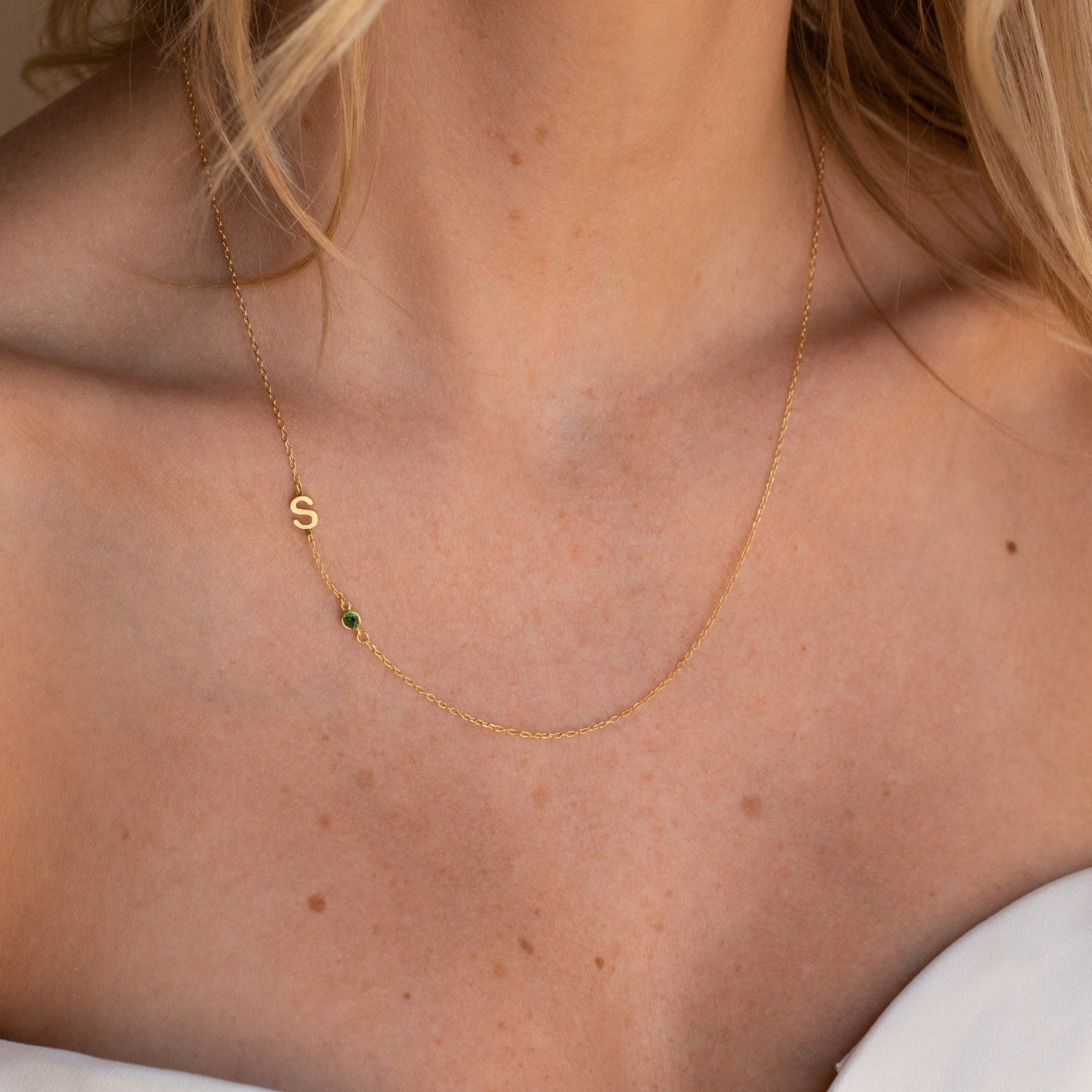 Sideways Initial Birthstone Necklace with an S charm and green stone, shown on a woman in a white off-shoulder top—a perfect Gift for Mom and stylish Personalized Letter Necklace.