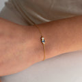 The Eloise Gemstone Bracelet, featuring a delicate chain and a small multicolored rectangular charm, rests gracefully on the wrist—perfect for fans of dainty jewelry.
