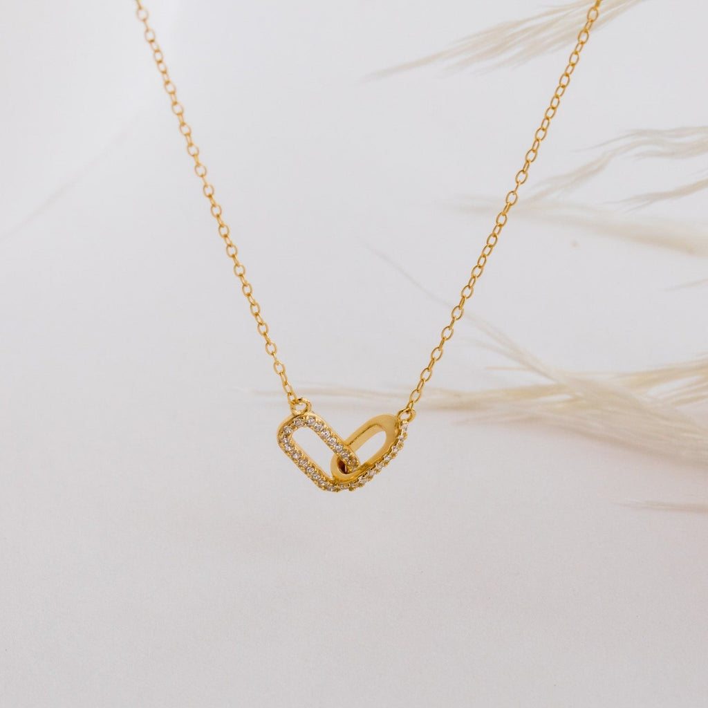 The Pave Linked Pendant Necklace features two interlocking gold links—one plain, one with sparkling stones—adding a glamorous touch to any look.