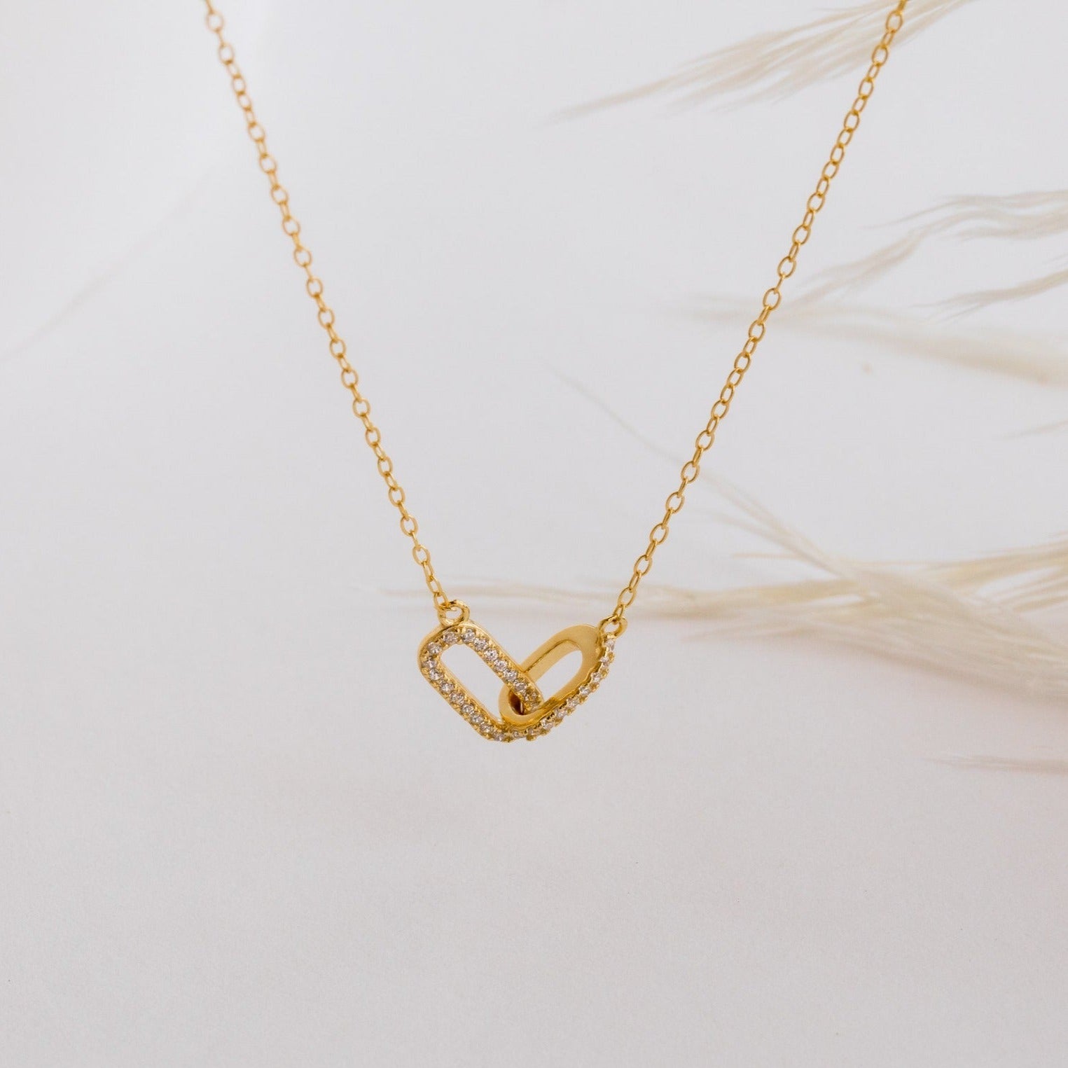 The Pave Linked Pendant Necklace features two interlocking gold links—one plain, one with sparkling stones—adding a glamorous touch to any look.