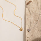 The Mandy Pave Butterfly Necklace, available in gold or silver and embellished with sparkling diamonds, is displayed on a textured cream and beige background.