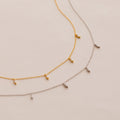 The Marquise Station Necklace, in both gold and silver, features a dainty chain adorned with small marquise-shaped diamond charms and is elegantly displayed on a light background.