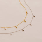 The Marquise Station Necklace, in both gold and silver, features a dainty chain adorned with small marquise-shaped diamond charms and is elegantly displayed on a light background.