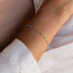 The Turquoise Station Bracelet, a delicate gold chain with small turquoise beads, is styled as a boho bracelet and pairs perfectly with a white long-sleeve shirt.