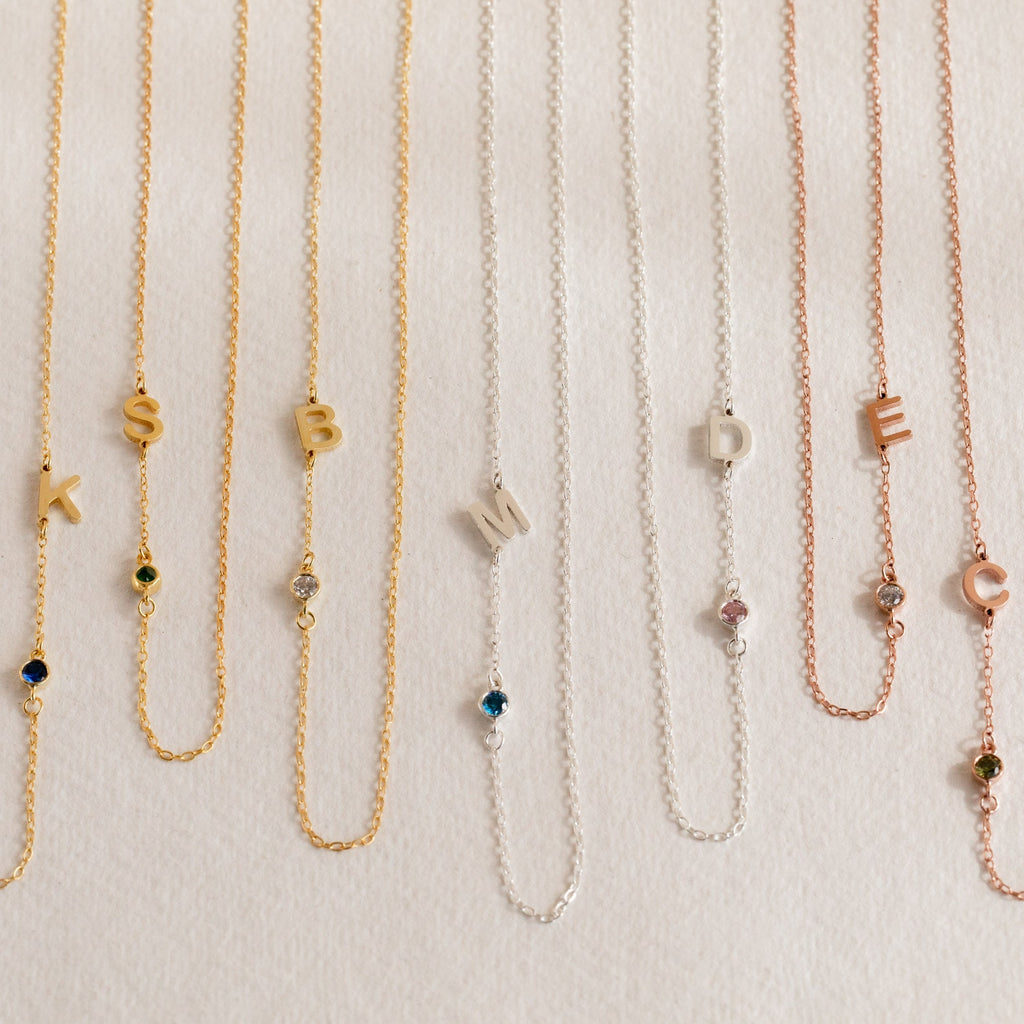 The Sideways Initial Birthstone Necklace features personalized letter pendants and delicate gemstone charms in gold, silver, or rose gold—an ideal gift for Mom.