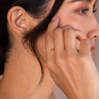 A woman touches her face, elegantly displaying the Aphrodite Pave Heart Ring on her finger, its sparkling diamond stones catching the light.