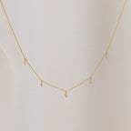 The Marquise Station Necklace features a delicate chain with small marquise-shaped diamond charms, displayed against a light fabric background.