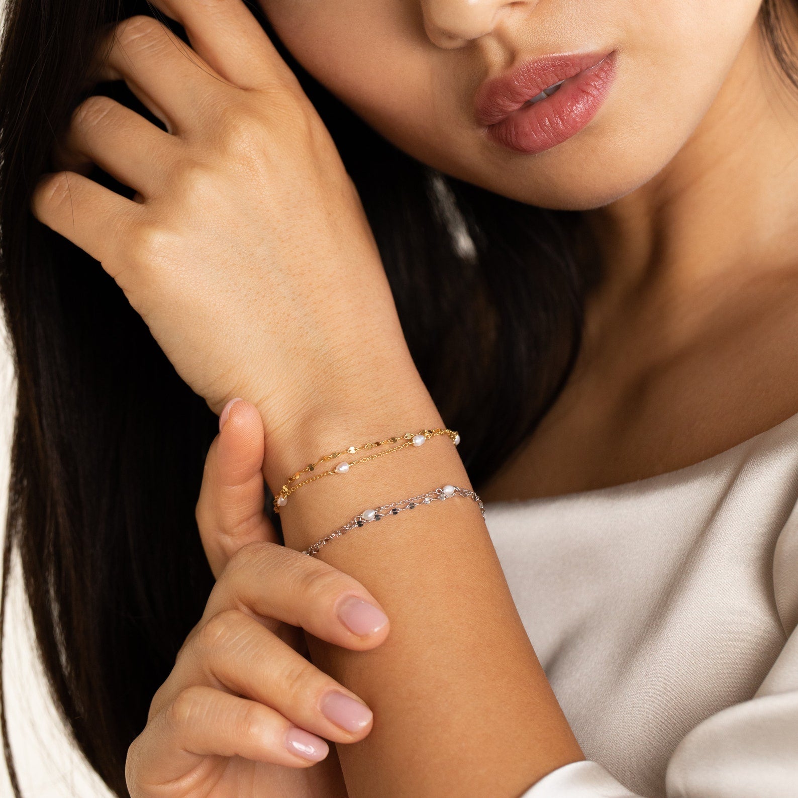 Lifestyle shot of model wearing magnolia wrapped bracelet in gold and silver styles with a neutral tone fabric to highlight vibrant gold tone and cool tone silver. 