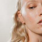 Close-up of a woman with wavy blonde hair wearing the Lucky Studs Set: a small gold hoop and a delicate wishbone earring in her left ear.