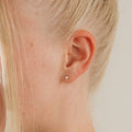 Close-up of a woman's ear with blonde hair wearing Opal Heart Studs—dainty, minimalistic earrings that add a subtle touch of elegance.
