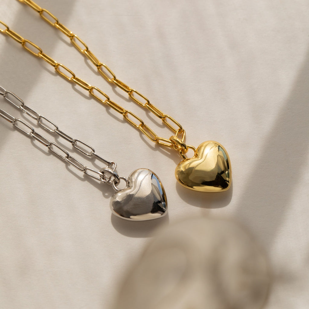 The Taylor Heart Paperclip Necklace features a heart-shaped pendant on a paperclip link chain, styled on a sunlit surface for a chic minimalist look.