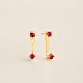 Straight‑on shot of a garnet pair gold birthstone ear jacket set—two small round CZ stones linked by a delicate bar—laid flat on a neutral background.