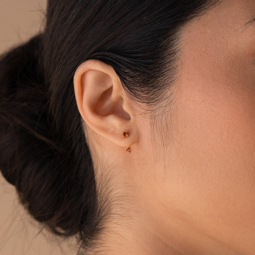 Close‑up of a model’s ear wearing a garnet gold birthstone ear jacket with its matching back‑facing CZ gemstone creating a layered look.