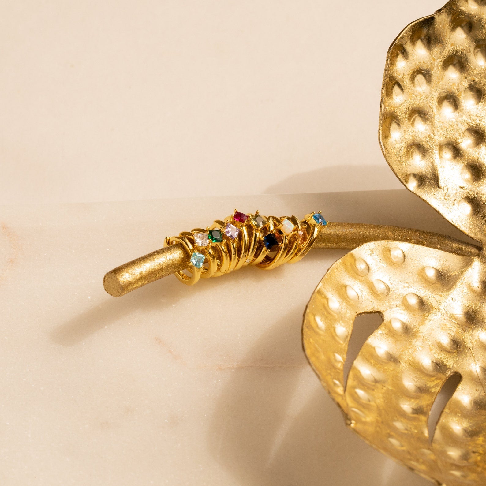 Athena Opal Huggies with vibrant gemstones stacked on a golden branch beside a decorative gold leaf.