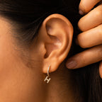 Close-up of an ear wearing Pave Initial Huggies in gold with diamonds, hand resting behind the ear—a sparkling, personalized touch and an elegant gift idea.