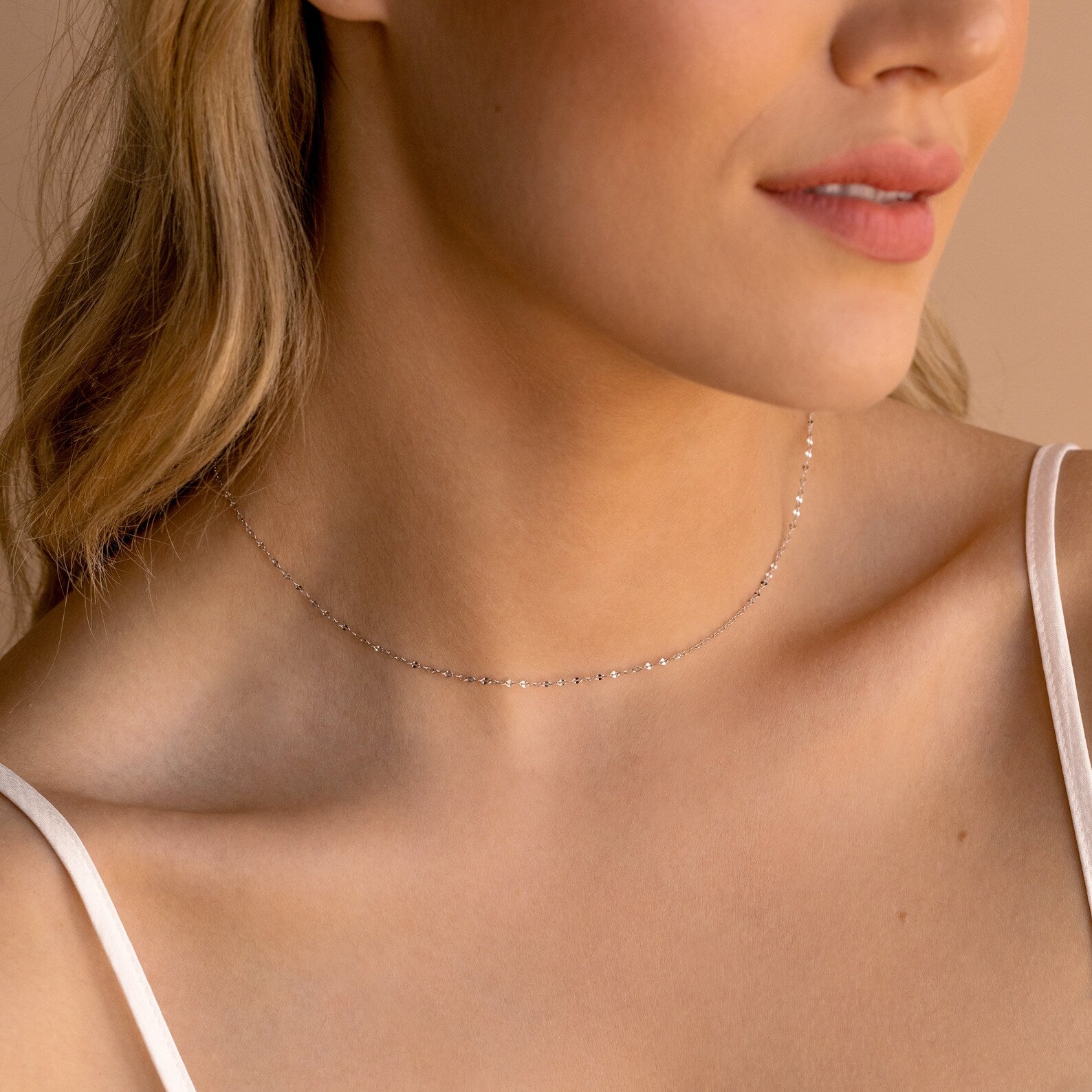 Woman wearing a delicate silver chain choker with small faceted links, styled with a white spaghetti strap top.