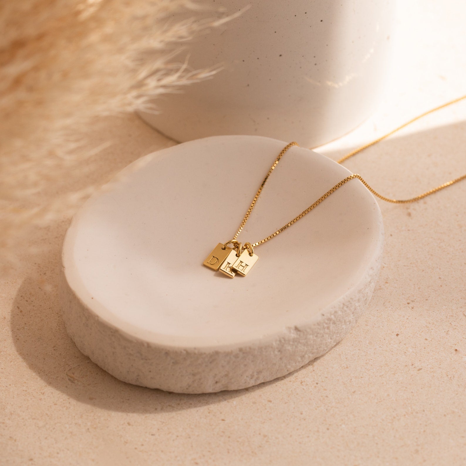 Mini Initial Tag Necklace with two small rectangular pendants displayed on a round white ceramic dish, softly lit—a personalized jewelry piece ideal for Christmas gifting.