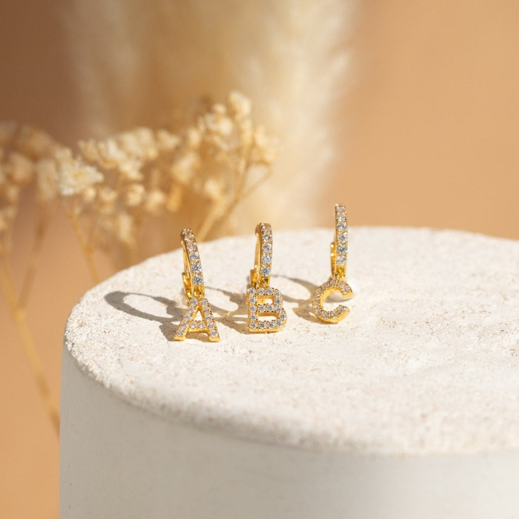 The Pave Initial Huggies are gold hoop earrings with diamond accents, each featuring a dangling A, B, or C initial—perfect personalized gifts that sparkle with pavé elegance.