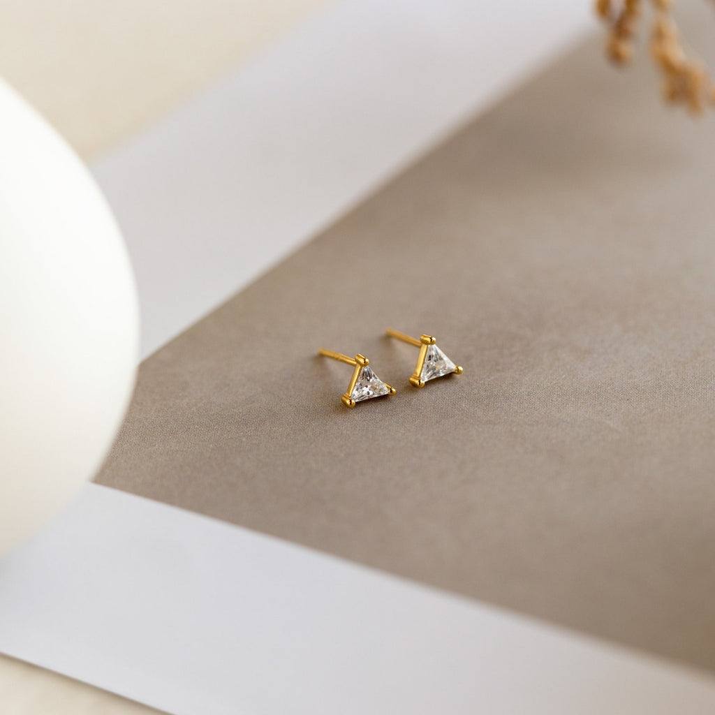 The Trixie Diamond Studs feature triangle-shaped diamonds set in gold and are displayed on a neutral, minimalist background—a modern classic that elevates any look.