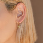 Close-up of an ear adorned with Astra Moon & Star Huggies: gold hoops featuring star and moon charms, accented with sparkling crystals.