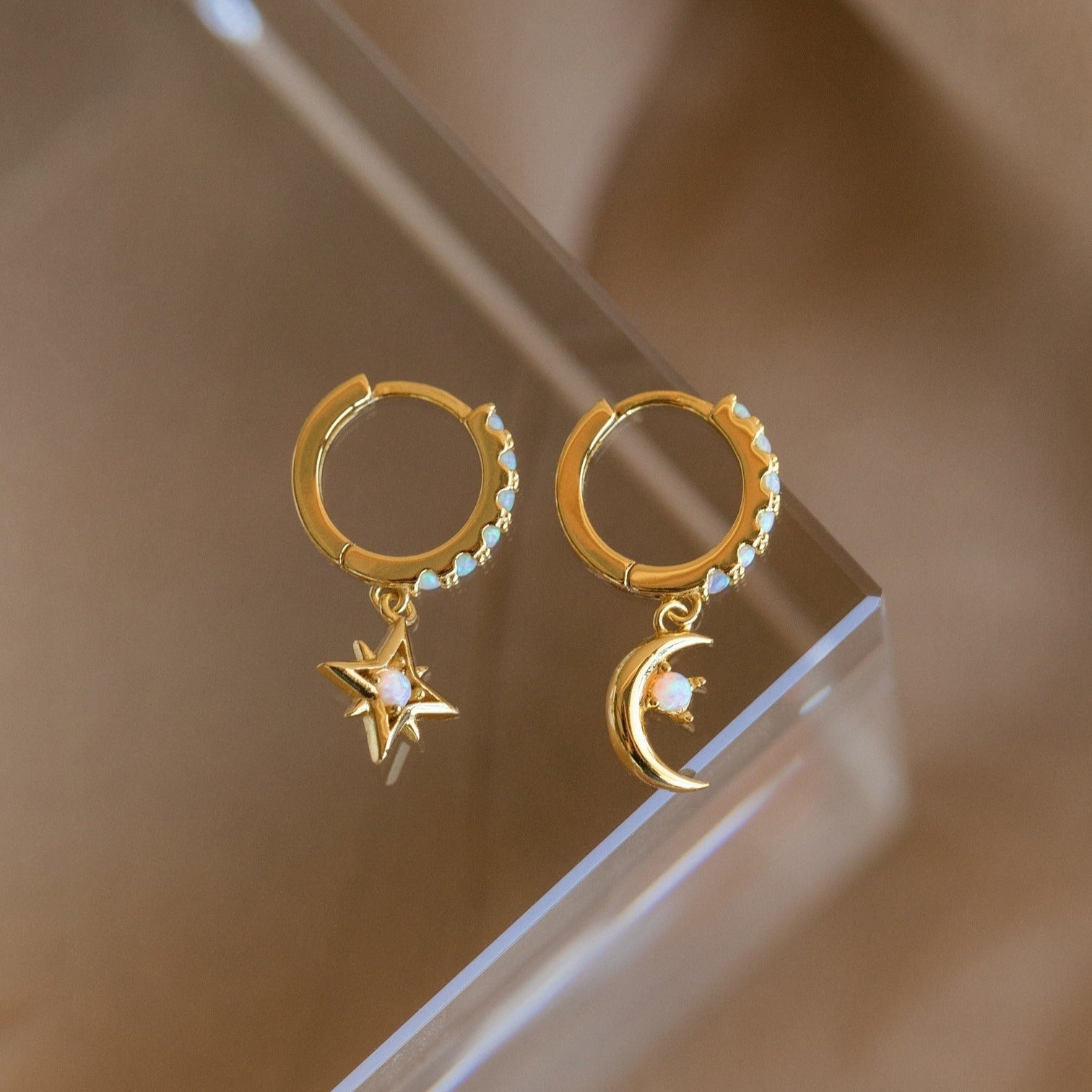 Astra Moon & Star Huggies: Gold hoops featuring a star on one earring and a moon on the other, each set with opal accents, bring celestial charm and radiant shine to any outfit.