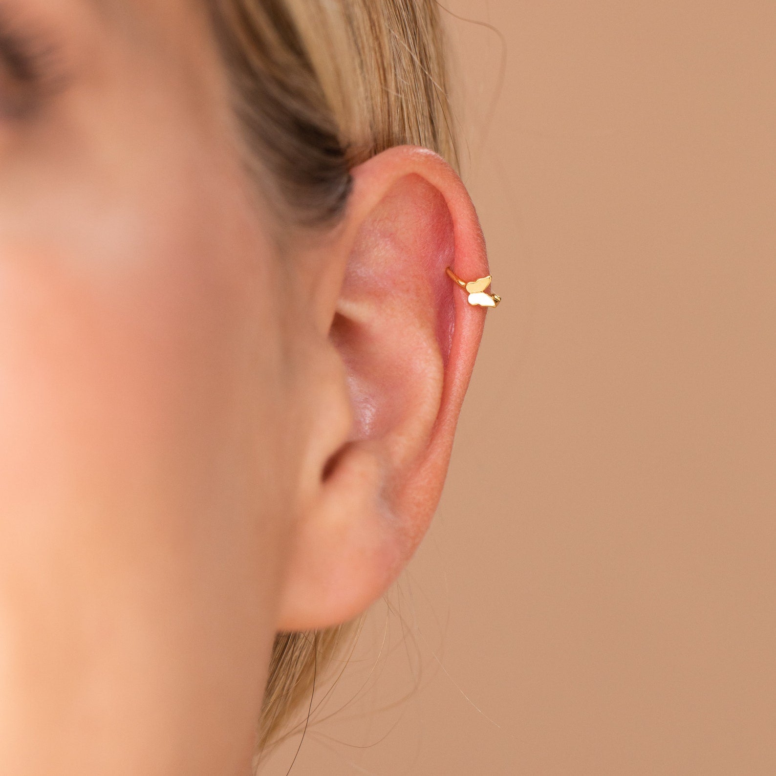 Close-up of dainty butterfly huggie hoop highlighting fitted clasp around ear.