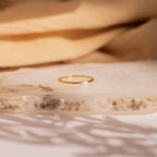 The Eloise Opal Ring, featuring a delicate gold band and a small iridescent opal gemstone, rests on a textured stone surface, embodying minimalist elegance.