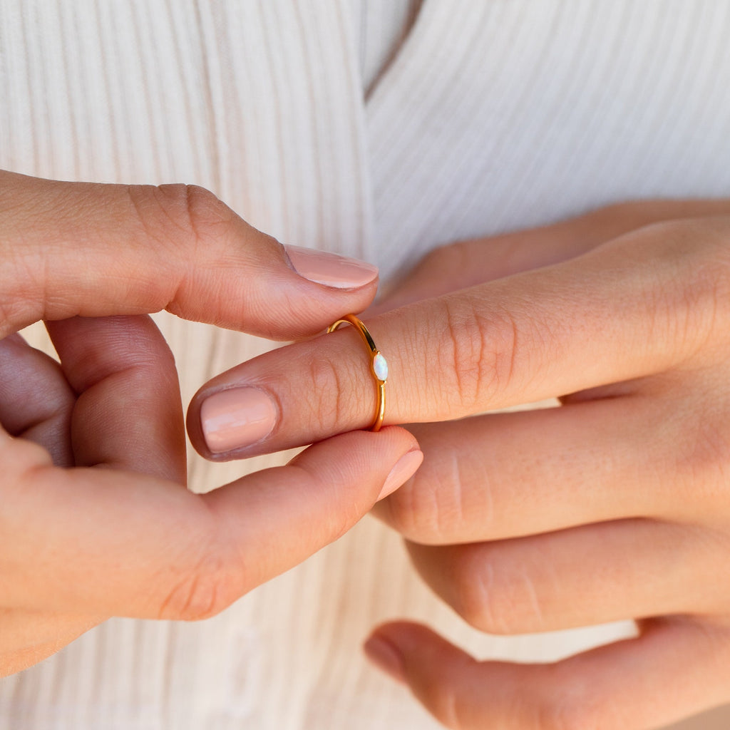A hand with nude nails slips on the Eloise Opal Ring—a thin gold band featuring a small iridescent opal, perfect for minimalists.