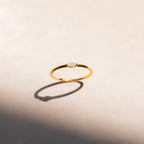 The Eloise Opal Ring features a delicate gold band and a small iridescent opal, casting subtle shadows on a light beige surface—a beautiful nod to minimalism.