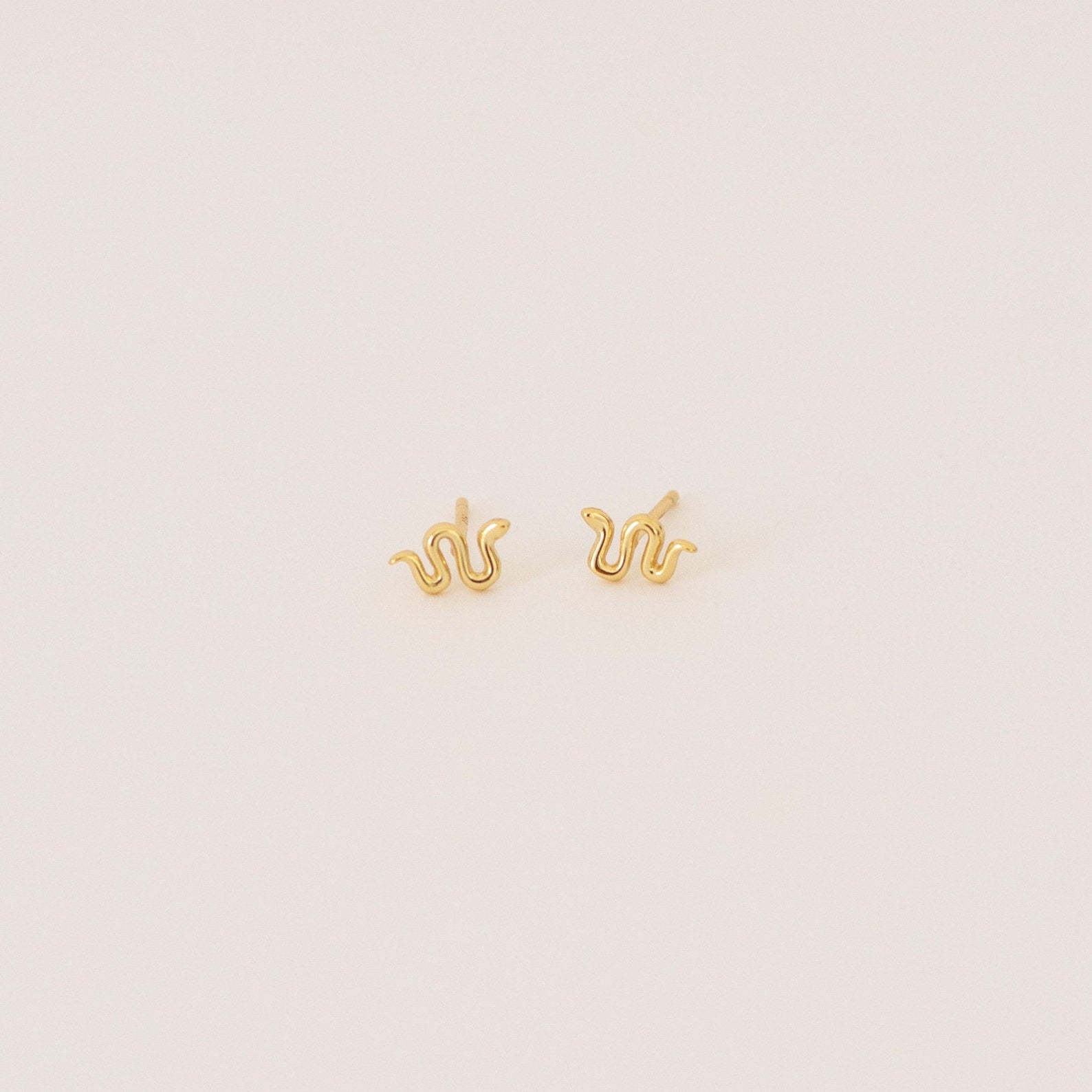 Tiny Python Studs: Small gold snake-shaped earrings that bring a boho-luxe accent to any outfit. Featured on a minimalist light background.