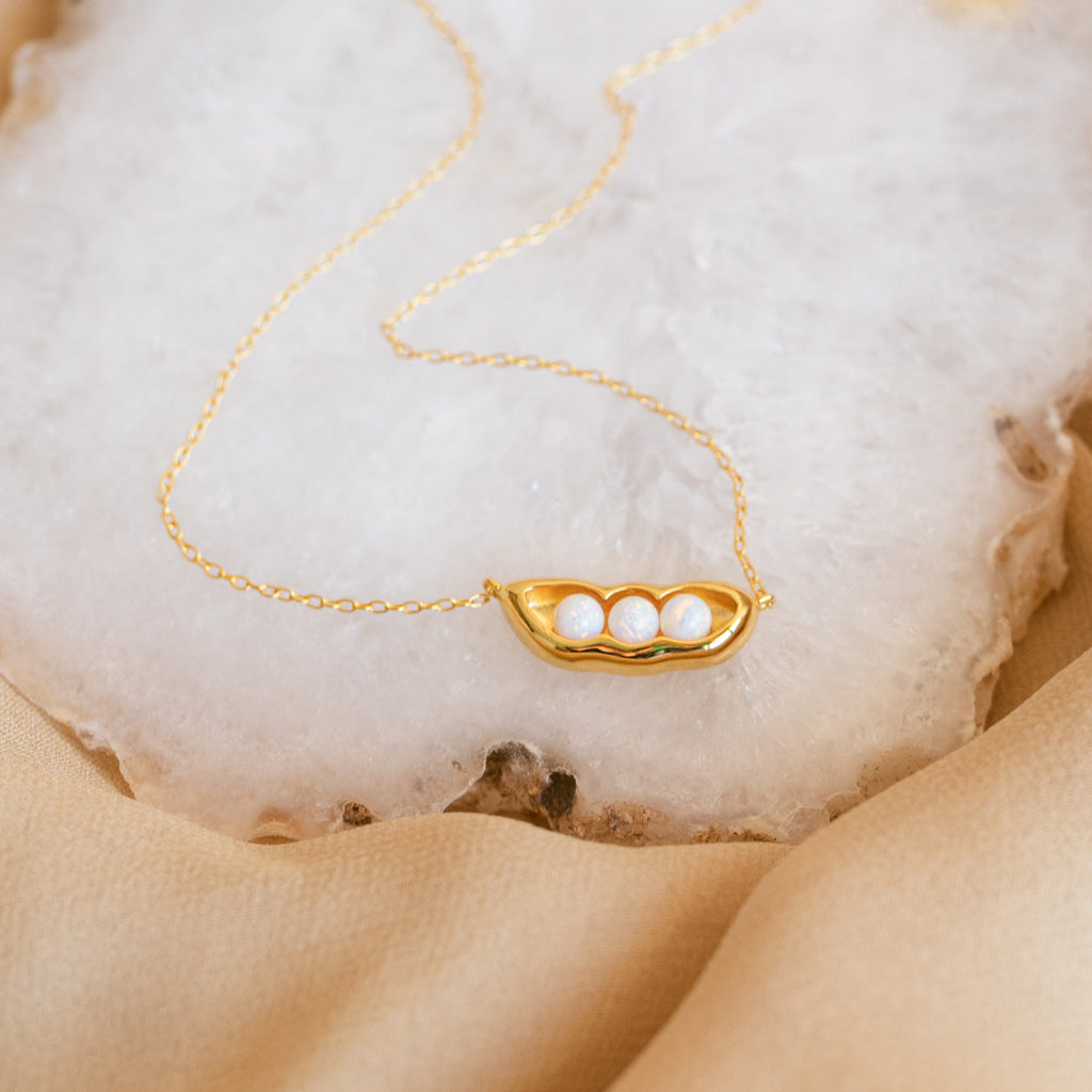 Peas in a Pod Necklace with a pendant of three white pearls, symbolizing unity and love—meaningful jewelry shown on a white stone surface.