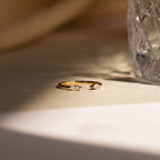 Celeste Duo Marquise Ring with two teardrop-shaped gemstones beside textured glass on a sunlit surface, highlighting its elegant open ring design.