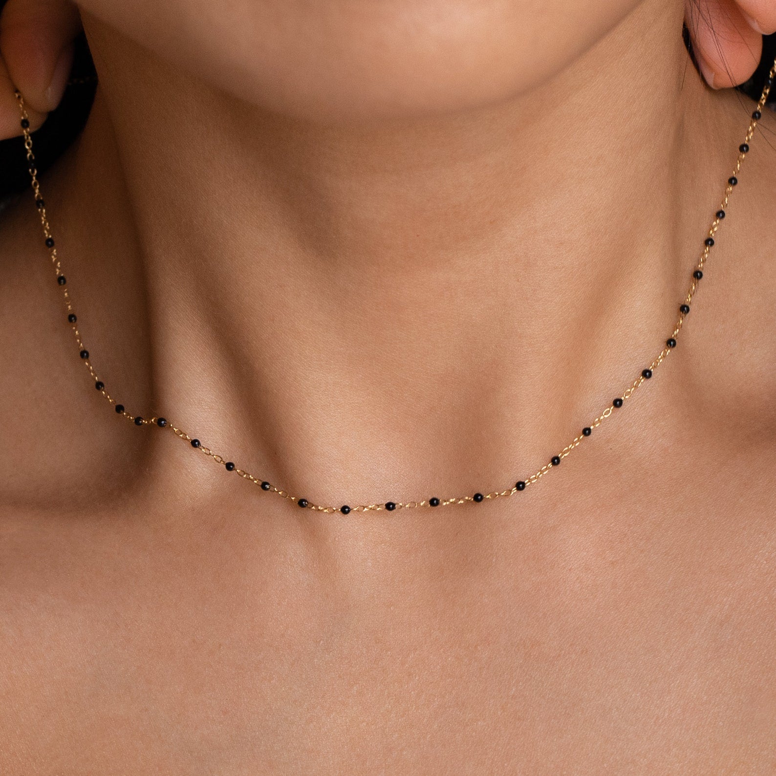Close-up of a woman wearing the Black Station Necklace—a delicate black and gold beaded piece that highlights an elegant fashion trend against bare skin.