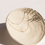 Gold and silver chain necklaces with evenly spaced small opal beads, displayed draped inside a textured cream ceramic bowl.