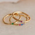 The Mini Birthstone Ring features a slim gold band set with vibrant gemstones, shown on a light marble surface—a delicate, elegant choice for everyday wear or as a personalized birthstone ring.