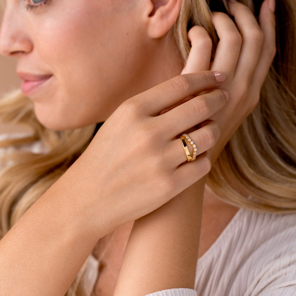 A woman touches her face and smiles softly, wearing the Wave Diamond Duo Ring on her finger.