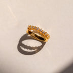 The Wave Diamond Duo Ring features a row of sparkling diamonds and casts an elegant shadow on a light surface.