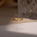 The Eloise Opal Ring, featuring a small iridescent stone, rests beside textured glass in soft lighting, capturing the essence of minimalism.