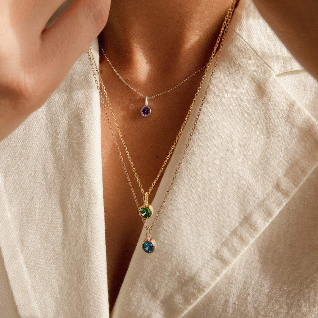 Close-up of dainty gold and silver Custom Birthstone Necklaces with colorful gemstone pendants, layered on someone in a cream blazer—an ideal choice for those who love meaningful jewelry.