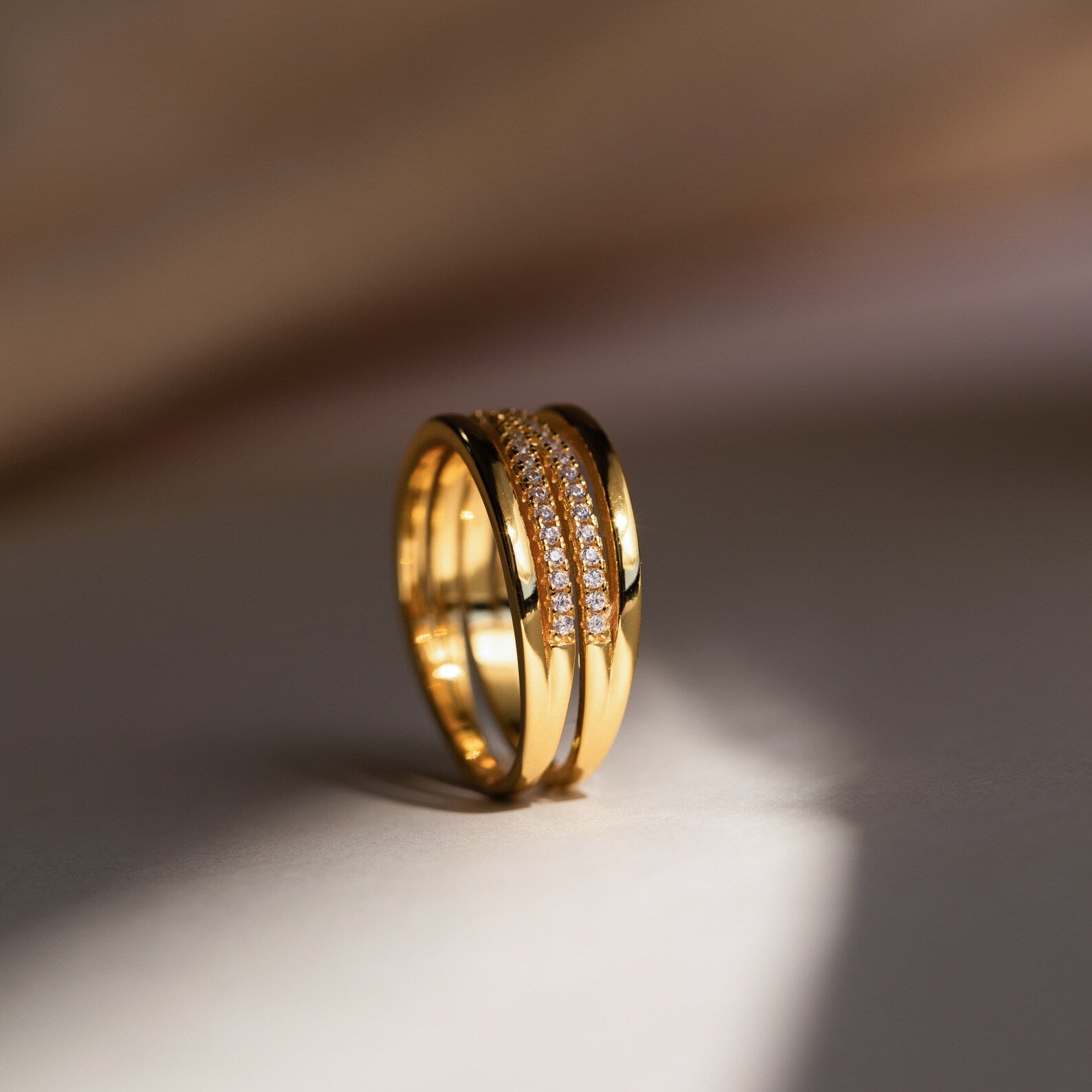 The Amani Pave Twist Ring, featuring a row of sparkling CZ diamonds, is showcased in soft, warm lighting on a neutral surface.