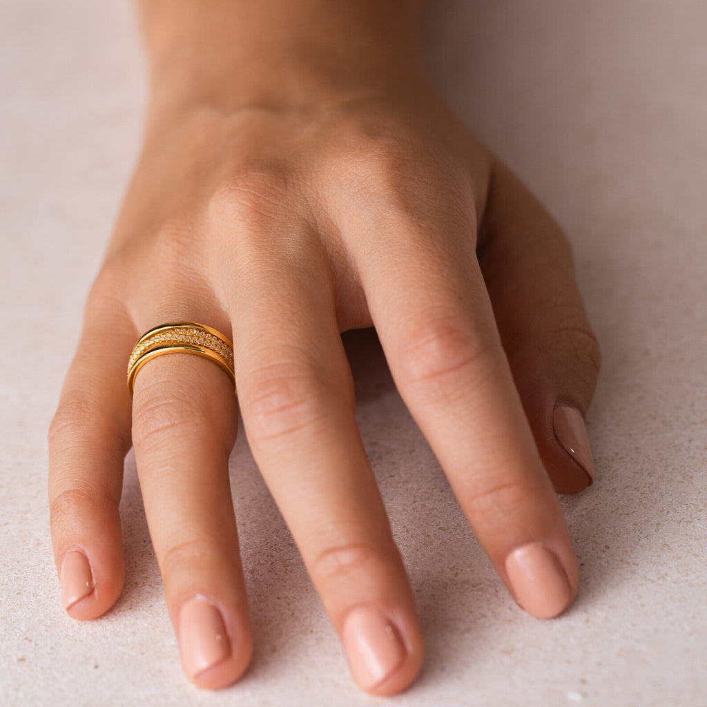 A hand with light pink nails wears the Amani Pave Twist Ring, a gold twist ring with small CZ diamonds, on the ring finger.