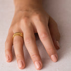 A hand with light pink nails wears the Amani Pave Twist Ring, a gold twist ring with small CZ diamonds, on the ring finger.