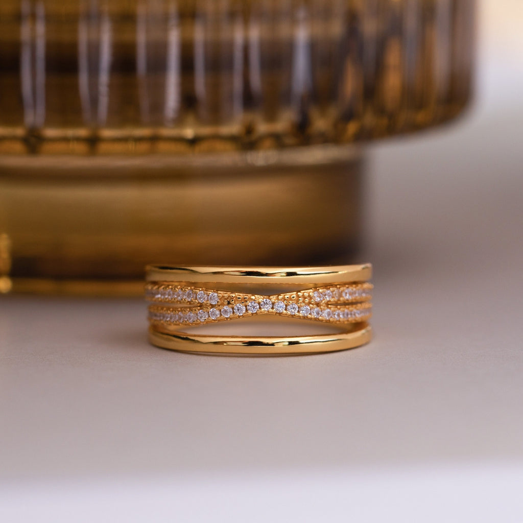 The Amani Pave Twist Ring features multiple intertwined gold bands, some adorned with sparkling CZ diamonds, displayed on a light surface.