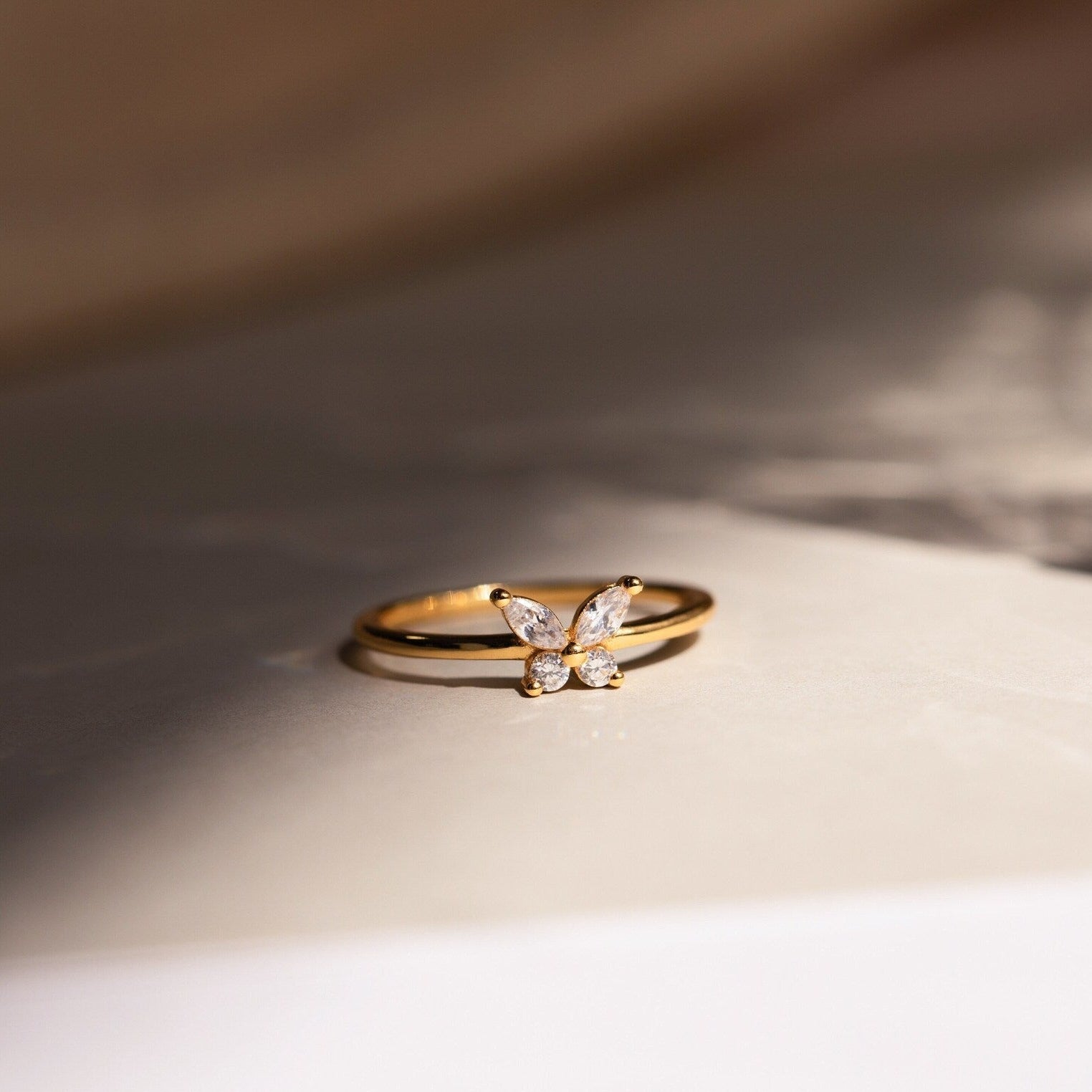 The Mariposa Diamond Ring features delicate butterfly wings set with sparkling CZ diamonds, resting on a light surface—an elegant symbol of enduring friendship.