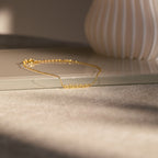 The Dainty Tiny Name Bracelet rests on a beige surface in soft natural light—ideal for fans of minimal jewelry and personalized gifts who love delicate, custom accessories.
