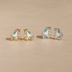 Unicorn Studs: Four pastel enamel unicorn earrings with gold edges on a beige surface—an adorable gift for girls who love whimsical jewelry.