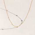 Delicate gold chain necklace with evenly spaced small opal beads, shown casting soft shadows on a light cream background.