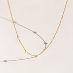 Delicate gold chain necklace with evenly spaced small opal beads, shown casting soft shadows on a light cream background.